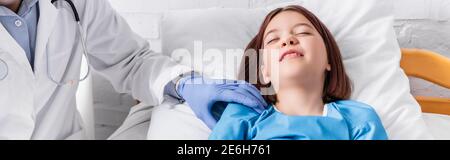 pediatrician examining sick girl lying in bed with closed eyes, banner Stock Photo