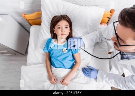 overhead view of girl lying in bed while doctor examining her with stethoscope Stock Photo