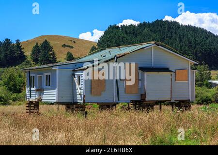 An empty house with boarded-up windows in the countryside, propped up on blocks for removal. Photographed in New Zealand Stock Photo