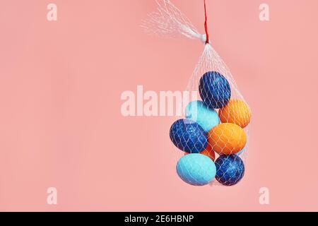 multi-colored chicken eggs in  bag mesh hang on pink background. easter Stock Photo