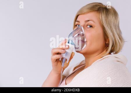 Senior woman using a nebulizer makes inhalation at home and looks at the camera. Empty space for advertising. Stock Photo