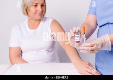 Senior woman and the hands of a nurse holding a syringe and a vaccine for covid 19. Fighting the spread of the virus on a white background. Stock Photo