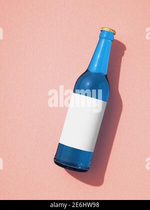 Single blue glass beer bottle laying on pink surface. Bottle with blank white label, shadow on background. Retro drink bottle concept. Stock Photo