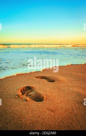 Vertical shot of human footprints on a wet sandy beach with a beautiful wavy seascape view Stock Photo