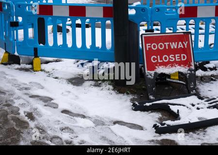 A footpath closed sign and barrier on an icy pavement / sidewalk covered with snow Stock Photo