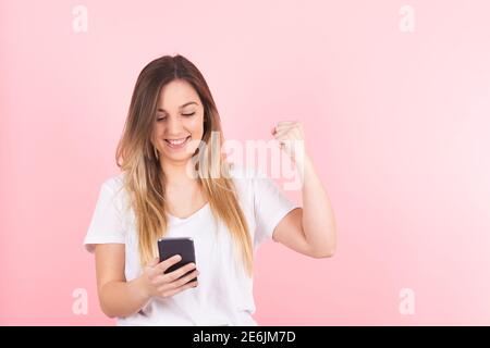 a young blonde woman looking at her cell phone makes a victory gesture Stock Photo