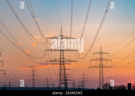 Electricity pylons and electric power transmission lines against vibrant orange sky at sunset. High Voltage towers provide power supply for good power Stock Photo