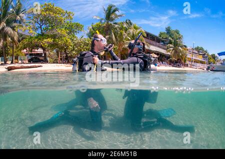 Scuba diver instructor with student during scuba teaching class on the beach half body in the water. West End, Roatan, Islas de la Bahia, Honduras Stock Photo