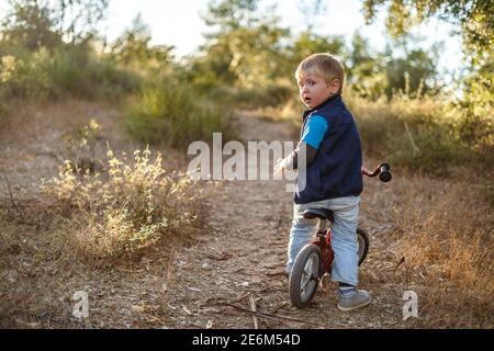 Adventurous three years old boy on his bicycle on the path in nature Stock Photo