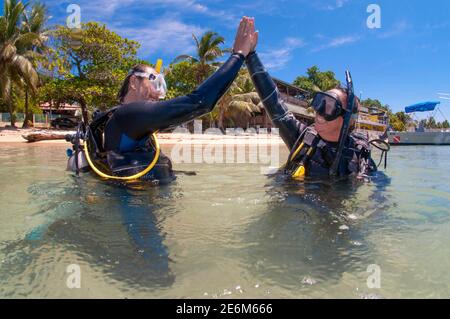 Scuba diver instructor with student during scuba teaching class with  half body in the water giving high five. West End, Roatan, Islas de la Bahia, Ho Stock Photo