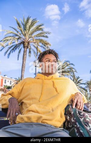 afro american black man with yellow sweatshirt looking at smartphone laying on a wooden bench in a park Stock Photo