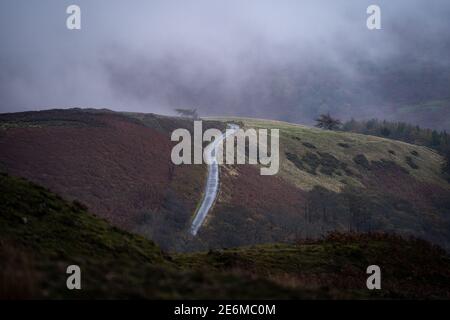 Country road lane leading to top of deserted hill mountain clouds foggy mist view baron landscape Peak District countryside dark moody fog cloud over Stock Photo