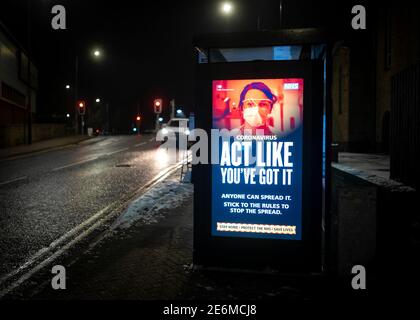 Coronavirus light up government warning information sign on bus stop shelter with cars passing at night in darkness lit up illuminated Covid 19 act Stock Photo