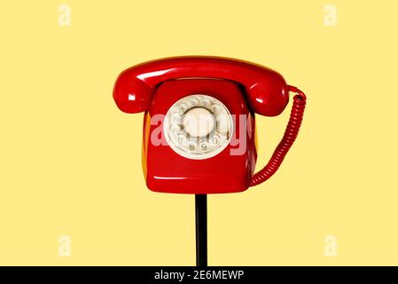 a red landline rotary dial telephone on the top of a black tubular stand, on a yellow background Stock Photo