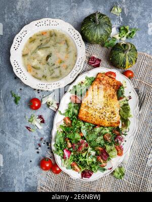 Salmon spiced with herbs, a plate of vegetable soup and a fresh salad. Healthy food Stock Photo