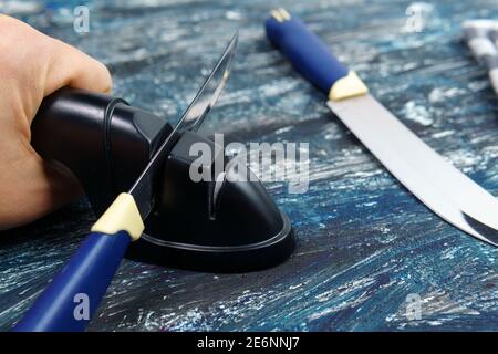 Sharpening a knife. Close-up of a man using a sharpener to sharpen a knife blade. Stock Photo