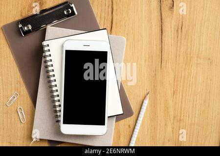 Stack of paper notebooks, clipboard and smartphone on wooden office desk table. Flat lay, top view. Stock Photo