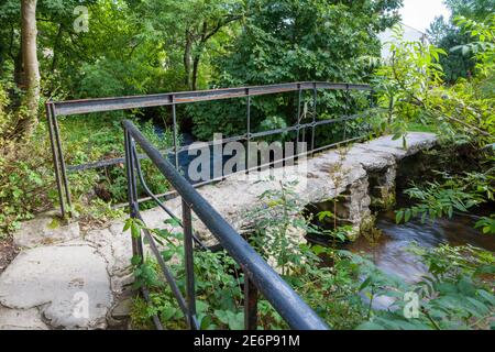 Summer view of a clapper style footbridge over Malham Beck in Malham village, Yorkshire Dales Stock Photo