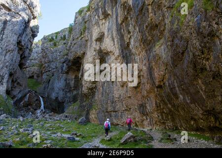 Two walkers on a path at Gordale Scar, an impressive limestone gorge near Malham in the Yorkshire Dales Stock Photo