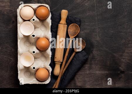 Baking and culinary background. Multicolored chicken eggs and shells in old cellulose vintage container with flour, sugar, wooden spoons and a rolling Stock Photo