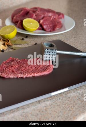 Computer Beef Computer is used as a kitchen board. Meat on laptop is ready to beat ...