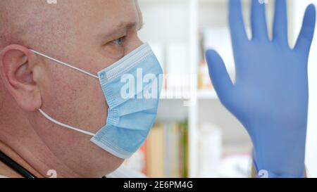Doctor Wearing Protective Face Mask, Puts Surgical Gloves on His Hands. Stock Photo