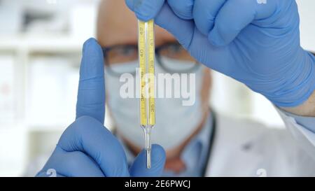 Doctor Wearing Protection Gloves and Face Mask Keep in His Hand a Medical Thermometer Stock Photo