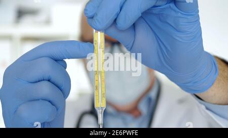 Doctor Wearing Protection Gloves and Face Mask Keep in His Hand a Medical Thermometer Stock Photo