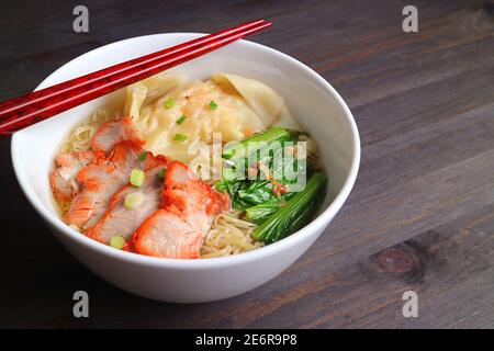 Closeup a Bowl of Wonton Dumpling and Egg Noodle Soup with Roasted Pork Isolated on Wooden Table Stock Photo