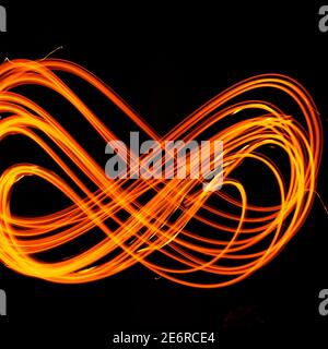 Drawing shapes with fire at night, infinity sign, bright colors on night background, fun with fire. Abstract fiery pattern in the shape of the number Stock Photo