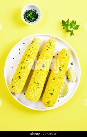 Boiled corn cobs on plate over yellow background. Top view, flat lay, close up Stock Photo
