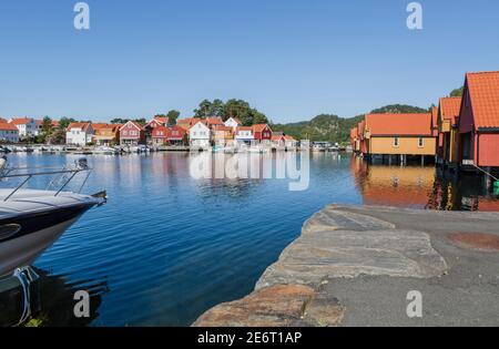 Blue and white small yacht and colorful houses at the port of the beautiful fishing village Svenevig in Southern Norway Stock Photo