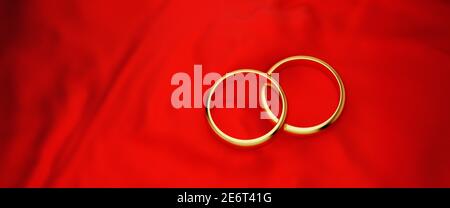 Two golden wedding rings on a red cloth background. Web banner size. Stock Photo