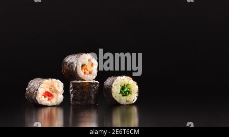 Background with four assorted vegetable maki sushi on dark wooden table with black background. Front view. Horizontal composition. Stock Photo