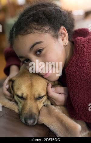 Portrait of biracial eleven year-old girl snuggling a small brown dog Stock Photo