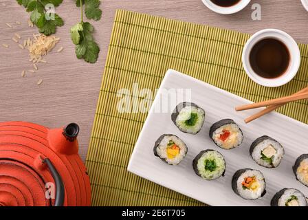 Detail of assorted sushi maki on white plate on wooden table with bamboo tablecloth. Top view. Horizontal composition. Stock Photo