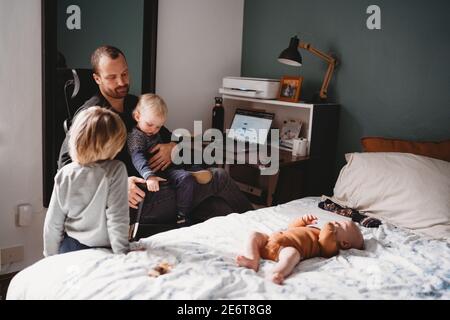 Kids on top of dad who is trying to work while from home during covid Stock Photo