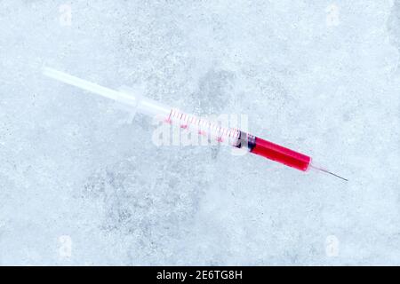 vaccine in a syringe with a needle with a red medical product for vaccination against coronavirus disease chilled to subzero temperatures lying on col Stock Photo