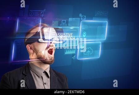Businessman looking through Virtual Reality glasses with ASSISTIVE TECHNOLOGY inscription, new technology concept Stock Photo