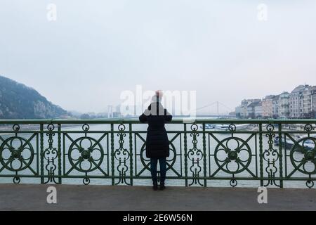 Behind a woman looking over the railing of the Liberty Bridge / Szabadsag Hid in Budapest on a cold winter day Stock Photo