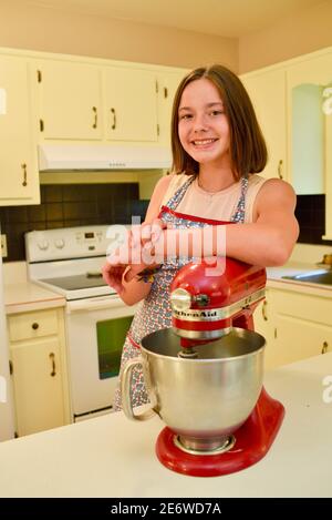 One, young attractive late teen caucasian women home baker smiling and leaning on red stand mixer in kitchen, Wisconsin, USA Stock Photo
