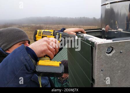 Facing a new chimney on a new two-story house, the worker uses a drill battery, does not enjoy protection, dressed in winter overalls 2020. Stock Photo