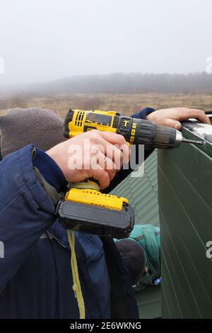 Facing a new chimney on a new two-story house, the worker uses a drill battery, does not enjoy protection, dressed in winter overalls 2020. Stock Photo