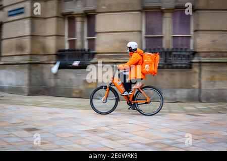 Just Eat delivery cyclist riding along a city pavement wearing a mask and helmet, UK Stock Photo