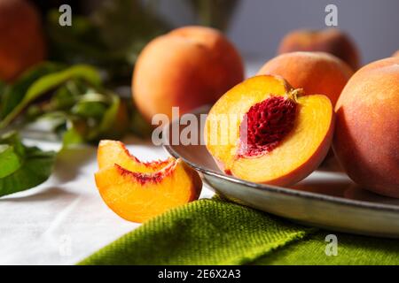 Peach in halves with bone. Peaches with leaves on color green plate on table with white tablecloth. Ripe juicy peaches Still life. Harvest of peaches Stock Photo