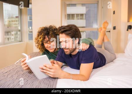 Closeup shot of a cute couple lying on a bed and reading an interesting book Stock Photo