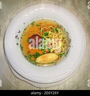 Traditional Austrian marriage soup in a white plate: beef broth with liver dumpling, sliced pancakes and semolina dumpling Stock Photo