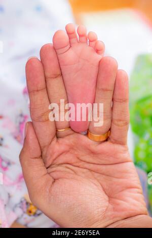 New born baby girls feet fit inside mothers fingers, three weeks old infant, pink small fingers, close up photograph. Mothers infinity love , warmth a Stock Photo