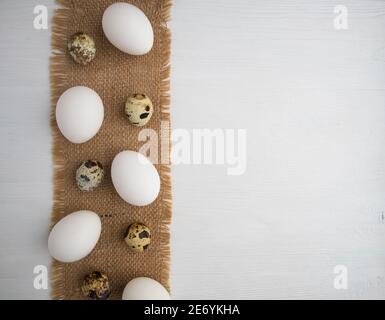 White chicken and quail eggs on a linen napkin on a white wooden background with space for text. Stock Photo