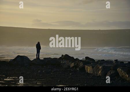 Sunrise seascape with a young man standing on the rocks of Doolin overlooking the Atlantic Ocean in County Clare, Dublin Ireland. Stock Photo